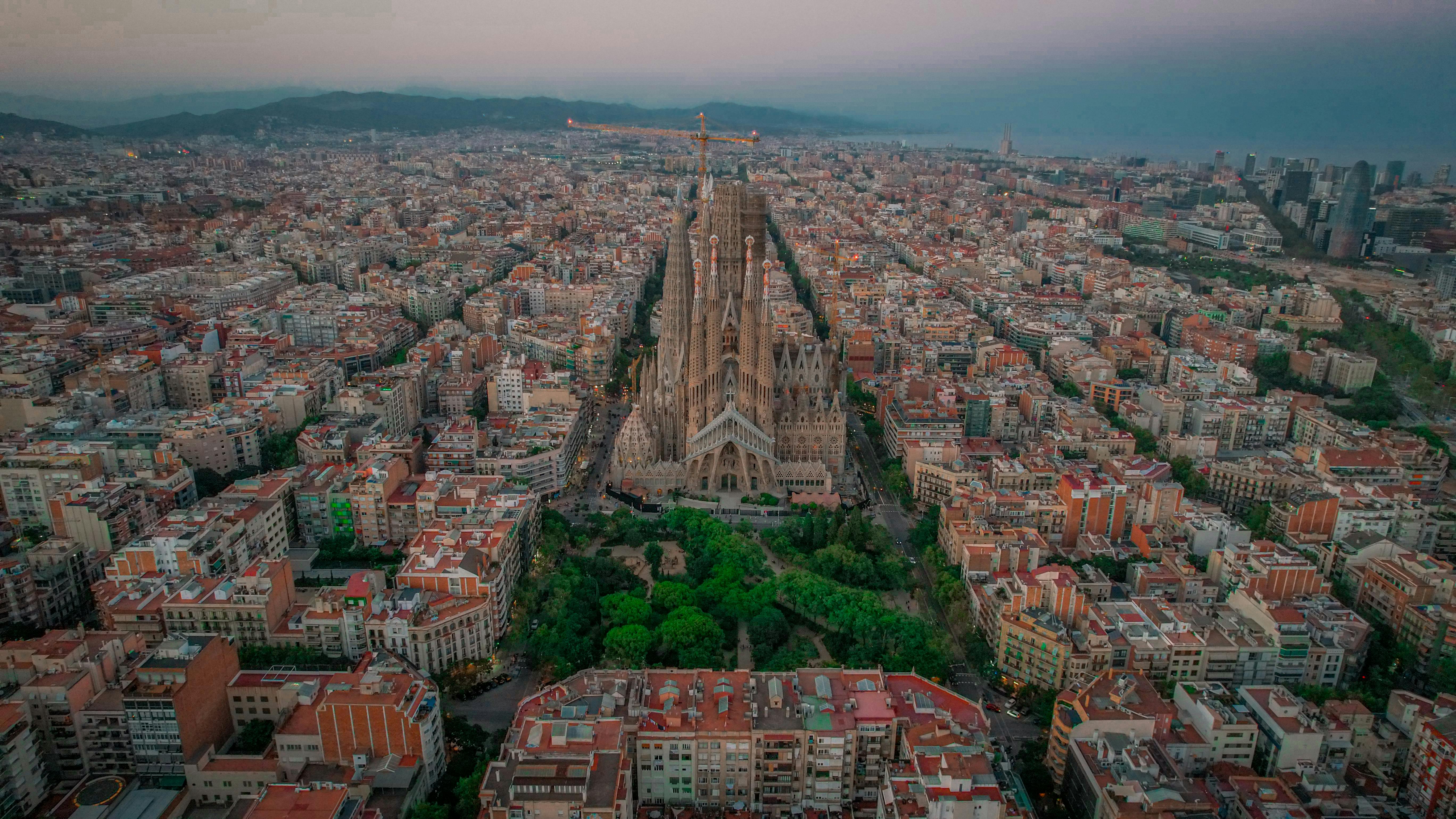 Panoramic aerial view of the Sagrada Família and Barcelona city grid at dusk, representing the host city for Mobile World Congress 2026.