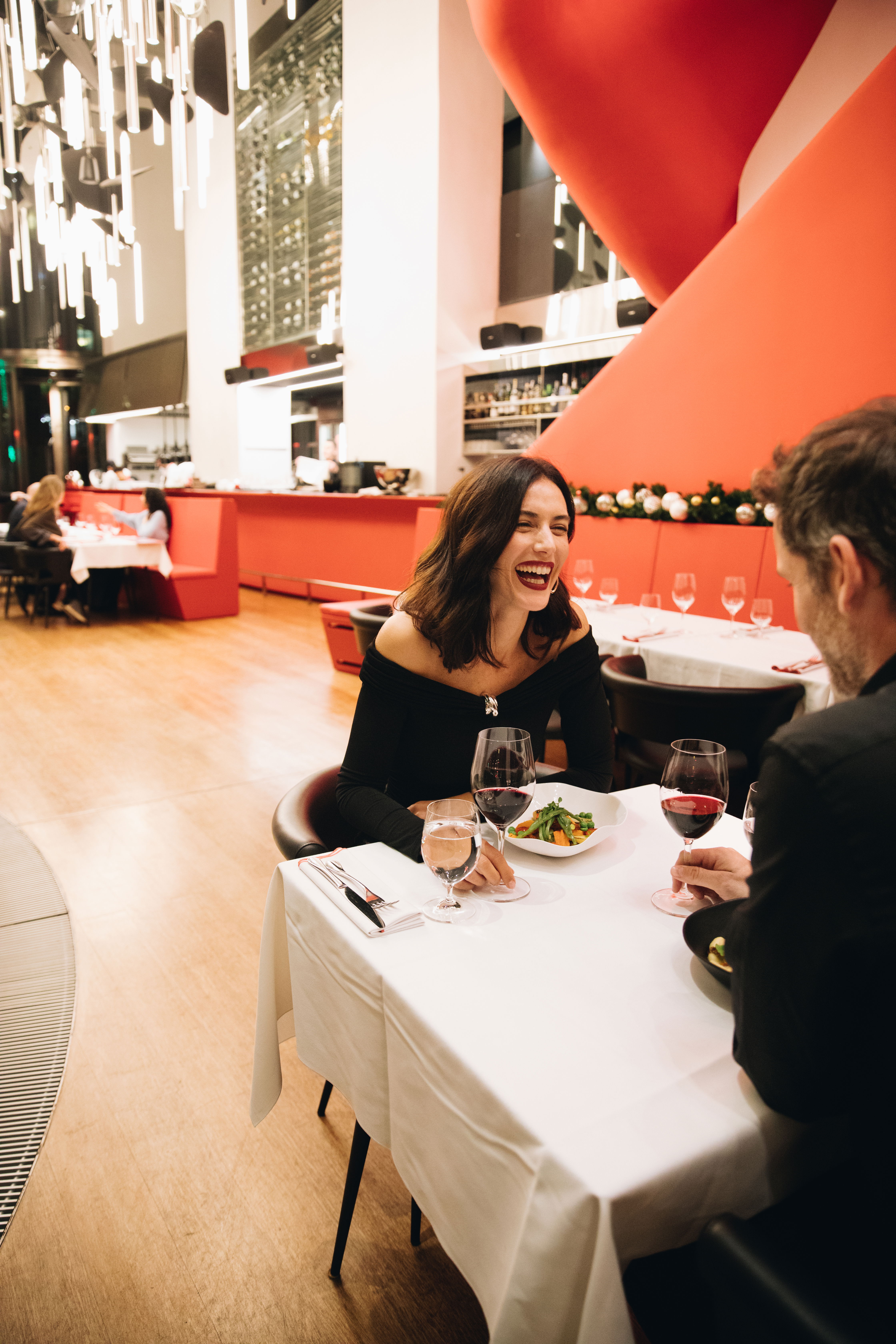 A woman laughing during a business dinner at Le Grand Cafe Rouge in Antares Barcelona, featuring the modern red interior and high ceilings designed by Odile Decq.