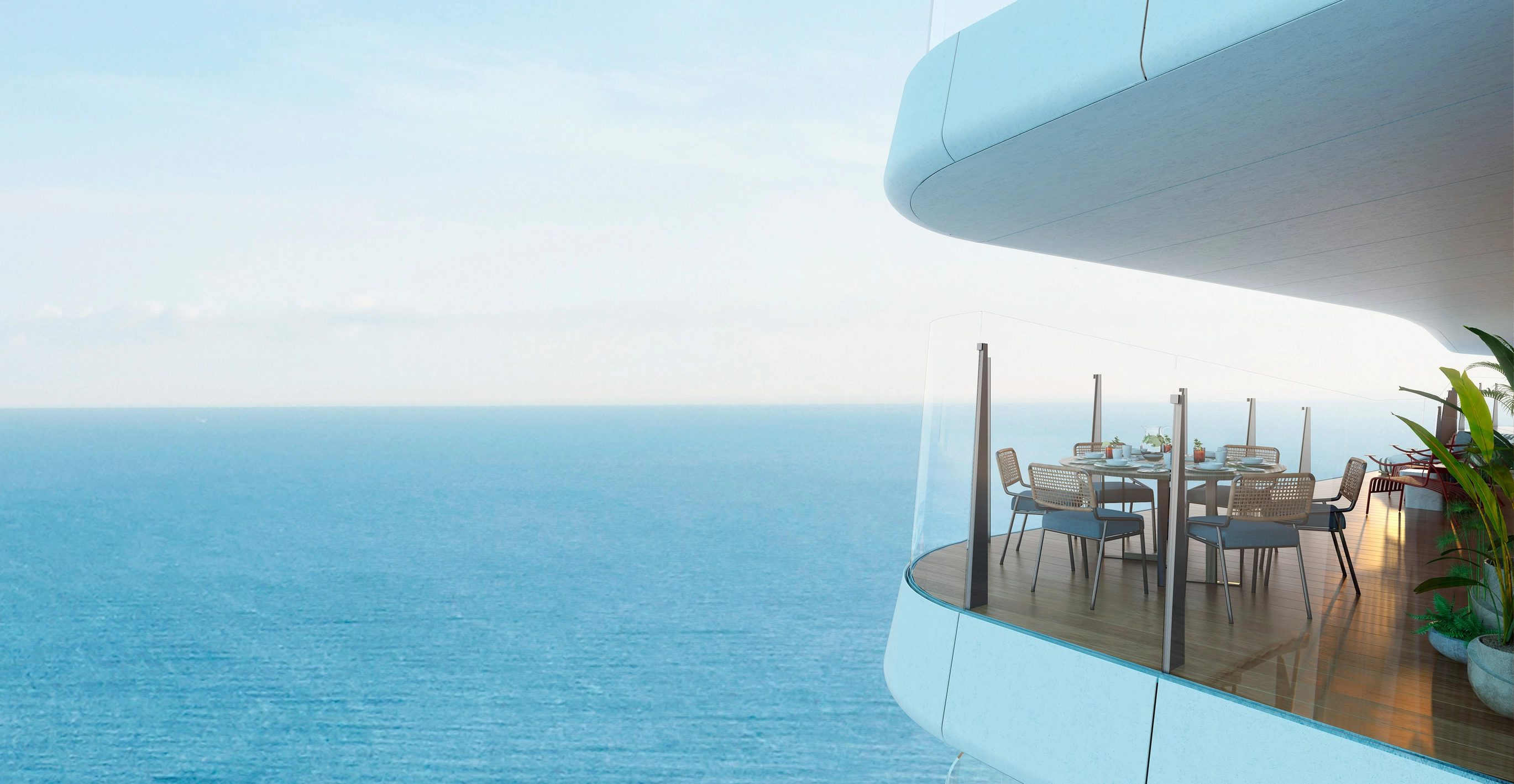 Close-up view of a curved terrace with wooden decking and modern dining furniture, featuring panoramic glass railings looking out over the endless Mediterranean Sea; showcasing the level of finish for effortless luxury living.