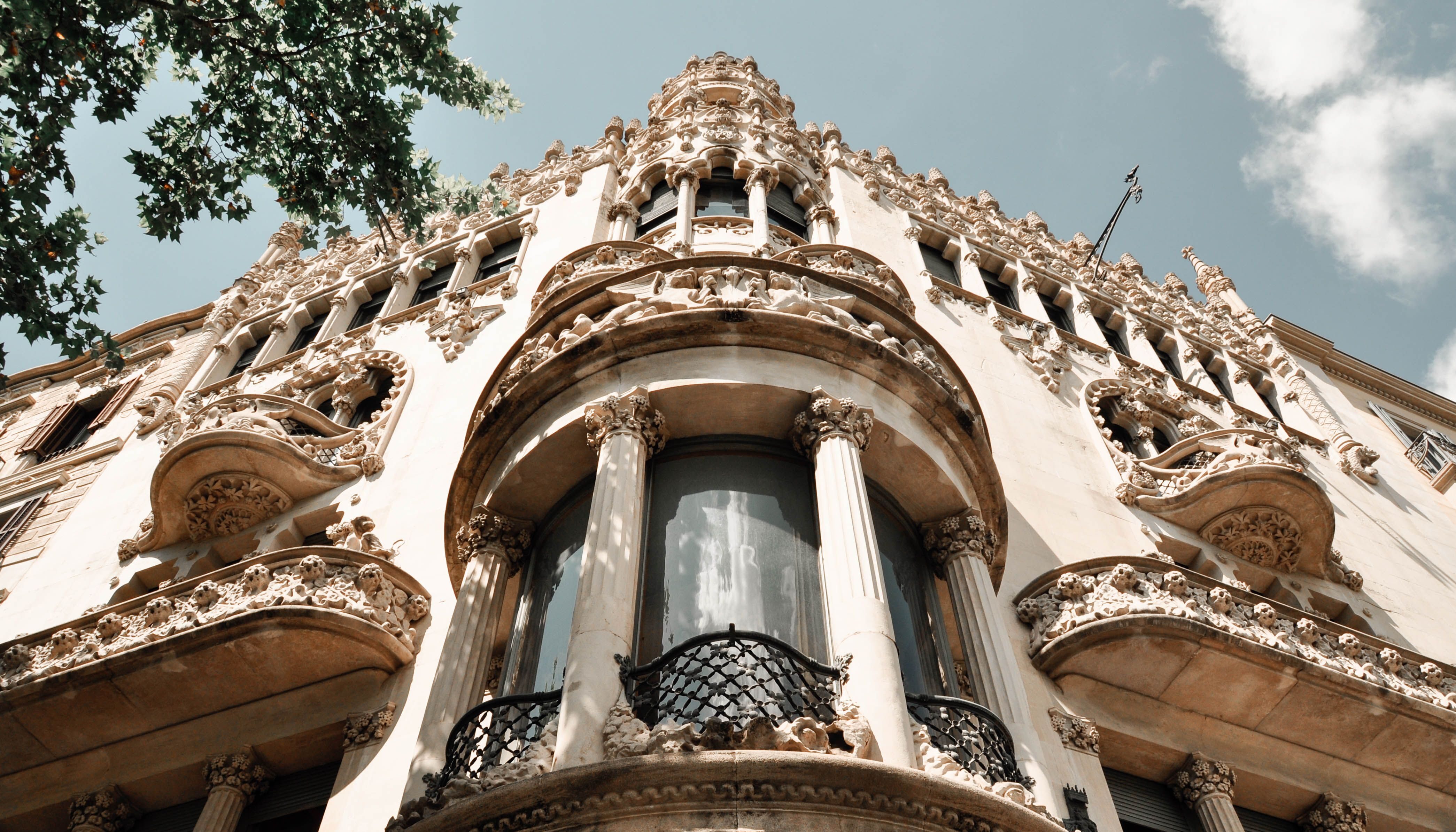 Low-angle view looking up at the ornate, highly detailed Catalan Modernisme facade of Casa Lleó i Morera, featuring intricate stone carvings, sculptural balconies, and elegant columns designed by Lluís Domènech i Montaner in Barcelona.