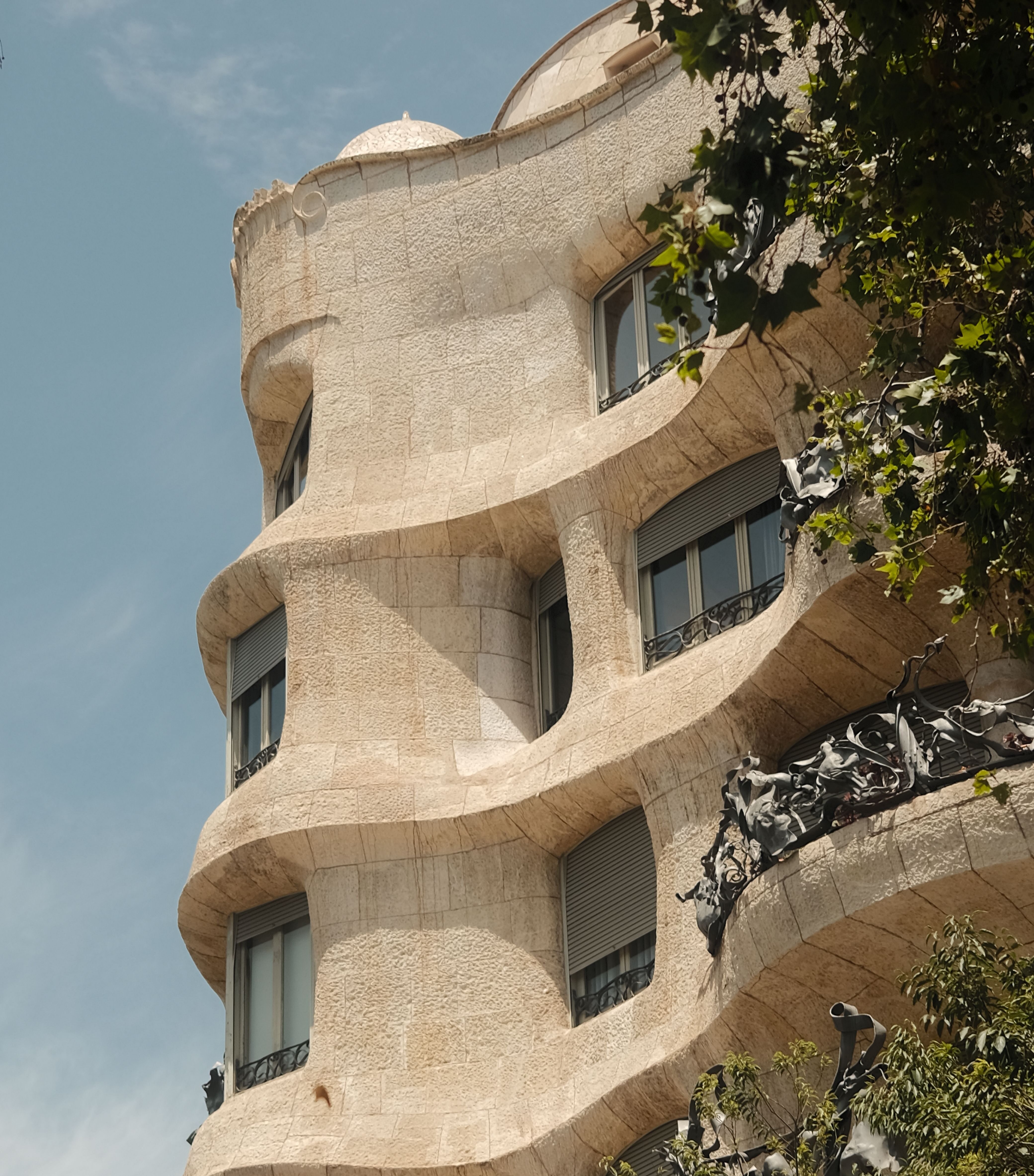 Low-angle view of the iconic undulating stone facade and organic, sculptural wrought-iron balconies of Casa Milà (La Pedrera) designed by Antoni Gaudí in Barcelona, captured against a clear blue sky.