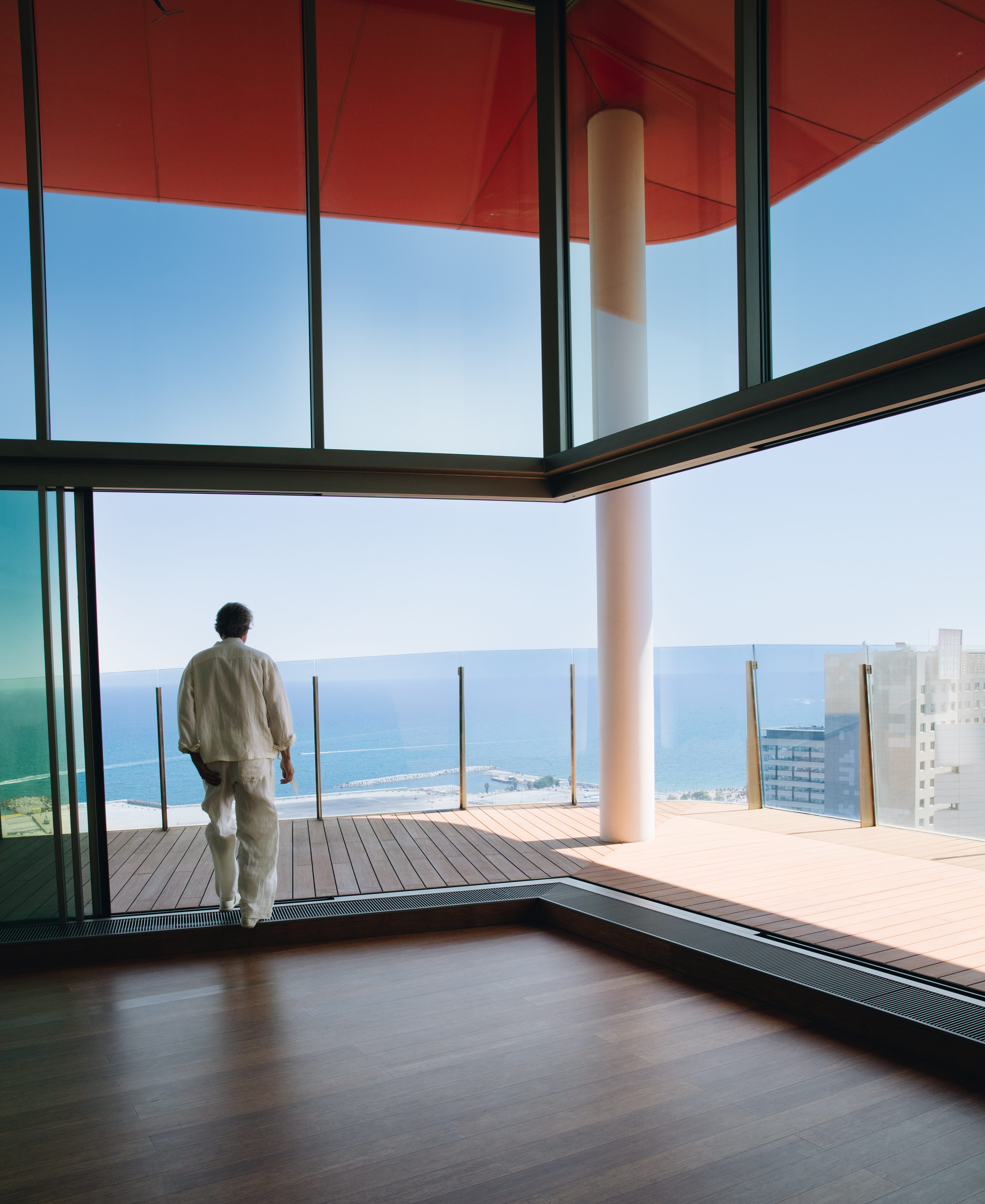 Man looking out from an Antares Barcelona penthouse terrace with floor-to-ceiling glass doors and panoramic Mediterranean Sea views, illustrating prime capital appreciation and generational wealth in the northern waterfront district.